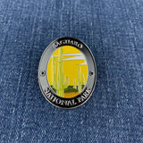 A medallion with an illustration of saguaro cacti and the text 'Saguaro National Park' meant to be affixed to a walking stick, displayed on a denim background