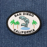 An oval-shaped patch featuring text 'SAN DIEGO CALIFORNIA' with an image of two dolphins and palm trees on a denim background