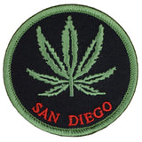 A round patch with a green cannabis leaf in the center and the text 'SAN DIEGO' at the bottom. The background is black.