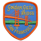 An embroidered shield-shaped patch featuring the Golden Gate Bridge over blue water with green hills, bordered in orange and labeled 'Golden Gate Bridge' and 'San Francisco' in yellow embroidery.