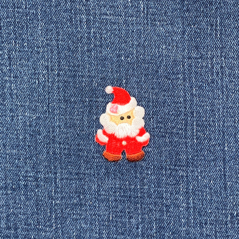 A embroidered Santa Claus applique patch with a red suit, white beard, and a brown base, designed for iron-on application on a denim background