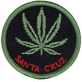 A round patch with a green cannabis leaf in the center and the text 'SANTA CRUZ' at the bottom. The background is black, and the text is in red.