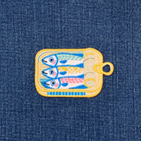 Embroidered patch of sardines in a can on denim fabric