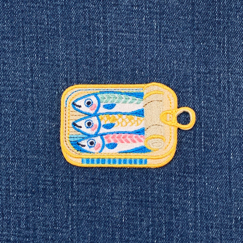 Embroidered patch of sardines in a can on denim fabric