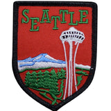 An embroidered shield-shaped patch featuring the word 'SEATTLE' in green letters above a red background with a white "needle" tower, blue mountain, and green trees.