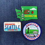 Three embroidered patches on a denim background: Washington state map, Seattle license plate, and Seattle cityscape.