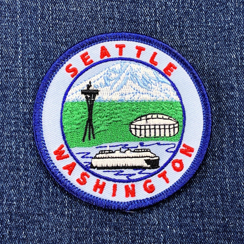 Circular souvenir patch for Seattle, Washington, showing Mount Rainier, the Space Needle, a ferry, and the stadium.