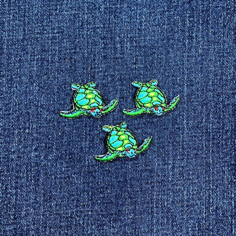 Three green sea turtle patches on a denim background