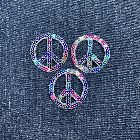 Three multicolored peace symbol patches on a denim background