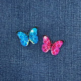 Two butterfly-shaped sequin patches, one blue and one pink, on a denim background.