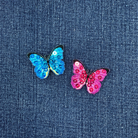 Two butterfly-shaped sequin patches, one blue and one pink, on a denim background.
