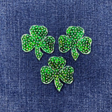 Three green shamrock patches on a denim background