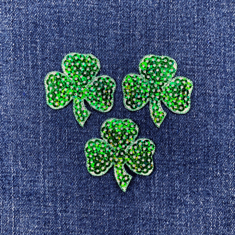 Three green shamrock patches on a denim background