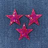 Three fuchsia glittery star-shaped patches on a denim background