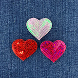 Three heart-shaped sequin patches in red, pink, and fuchsia on a denim background.
