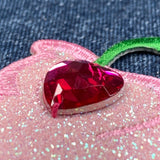 Heart-shaped red gemstone on a pink glittery surface with a denim background