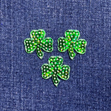 Three green sequin shamrock-shaped patches on a denim background