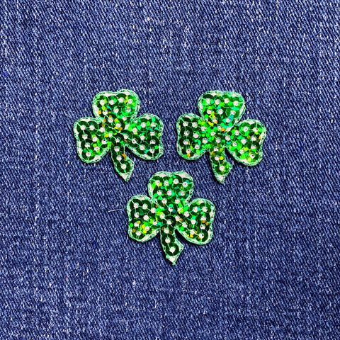Three green sequin shamrock-shaped patches on a denim background