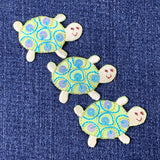 Three decorative turtle patches on a denim background