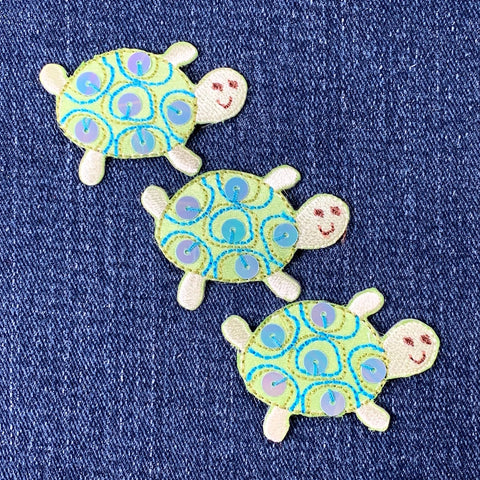 Three decorative turtle patches on a denim background