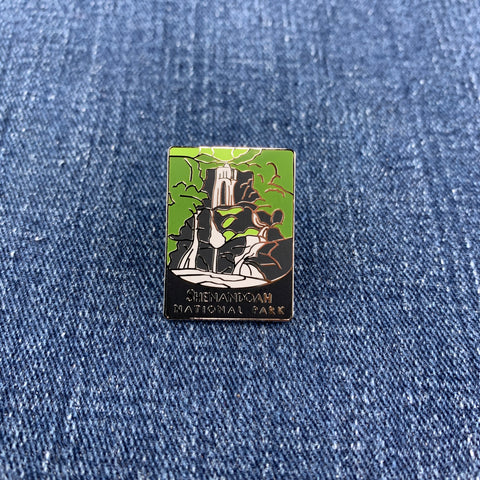 A collectible pin featuring an illustration of a waterfall with the text 'Shenandoah National Park' at the bottom on a denim background