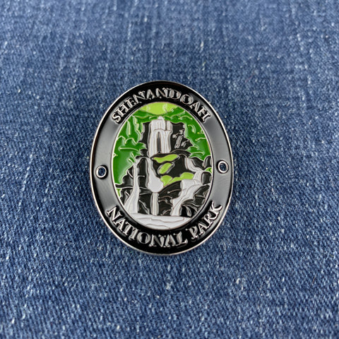 An oval enamel Walking Stick Medallion featuring Shenandoah National Park, displayed on a blue denim background.