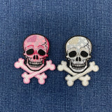 Pink skull and crossbones patch and silver skull and crossbones patch on denim fabric