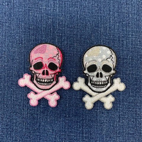 Pink skull and crossbones patch and silver skull and crossbones patch on denim fabric