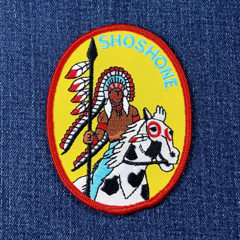 Patch with an illustration of a Native American chief on a horse, labeled 'Shoshone', on a blue denim background.