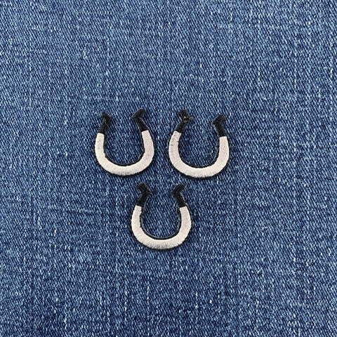 three silver and black horseshoe patches on a denim background