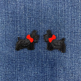 Two black dog-shaped patches with red bows on a denim background