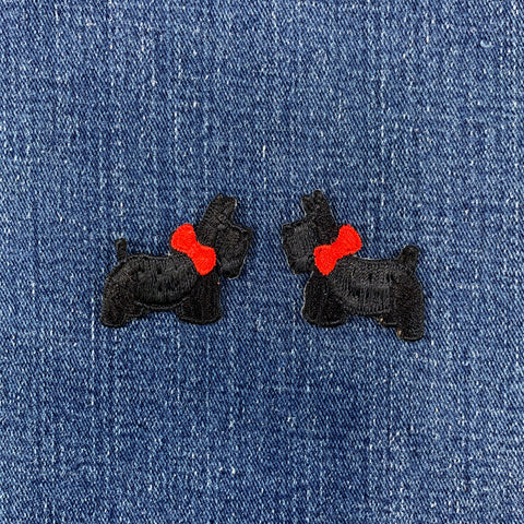Two black dog-shaped patches with red bows on a denim background