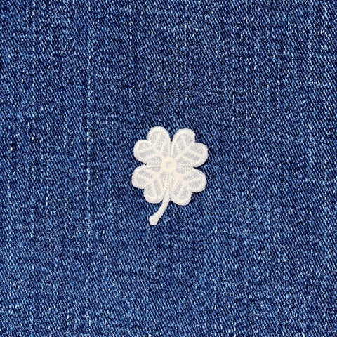 White embroidered four-leaf clover on blue denim fabric