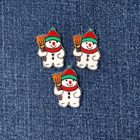 Three snowman patches with red hats and scarves on a denim background