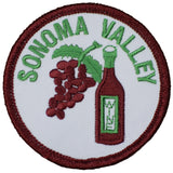 A circular embroidered patch on a white background, featuring a cluster of reddish-brown grapes, green leaves, and a maroon wine bottle with a green cap. The words 'SONOMA VALLEY' are stitched in bright green text around the top curve. The patch has a thick, dark red/maroon border.