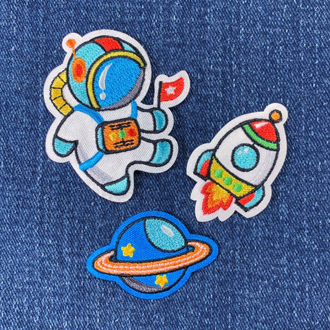 Set of space-themed patches including an astronaut, rocket, and planet on denim fabric.