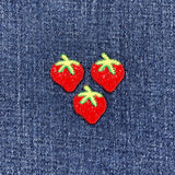 Three red strawberry patches with green leaves on a denim background