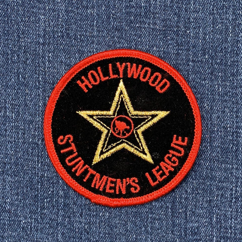 A round embroidered patch with the text 'Hollywood Stuntmen's League' and a star in gold on a black background with a red border on a denim background.