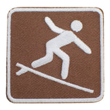 An embroidered square patch featuring a surfer on a brown textured background with a white border.
