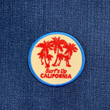 Round patch with palm trees and 'Surf's Up California' text on a blue denim background