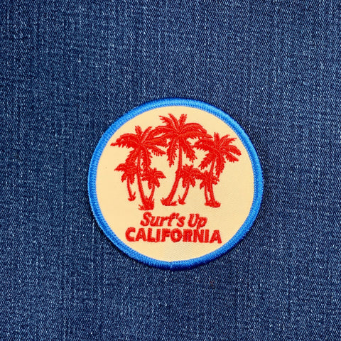 Round patch with palm trees and 'Surf's Up California' text on a blue denim background