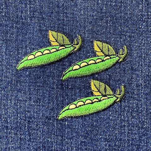 Three green embroidered pea pods on a denim background