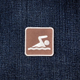 A square brown patch with a white swim icon, displayed on a dark blue denim fabric background.