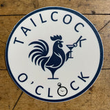 A circular sticker with a dark blue design on a white background. The center features the silhouette of a rooster (cock) holding a martini glass. The text 'TAILCOCK O'CLOCK' is curved around the design, with a small pocket watch graphic at the bottom.