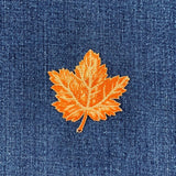 Embroidered orange leaf on blue denim fabric