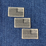 Three tan and black reverse American flag patches on a denim background
