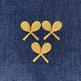 Three embroidered gold tennis racket patches on a blue denim background