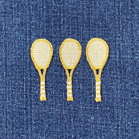 Three gold tennis racket patches on a denim background