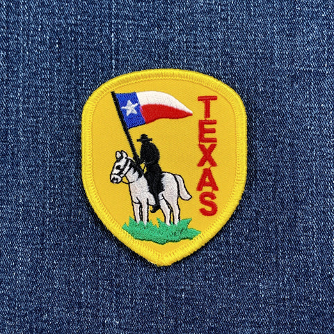 Embroidered patch of a cowboy on a horse with a Texas flag on a denim background