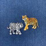 Two embroidered tiger patches on a blue denim fabric background.